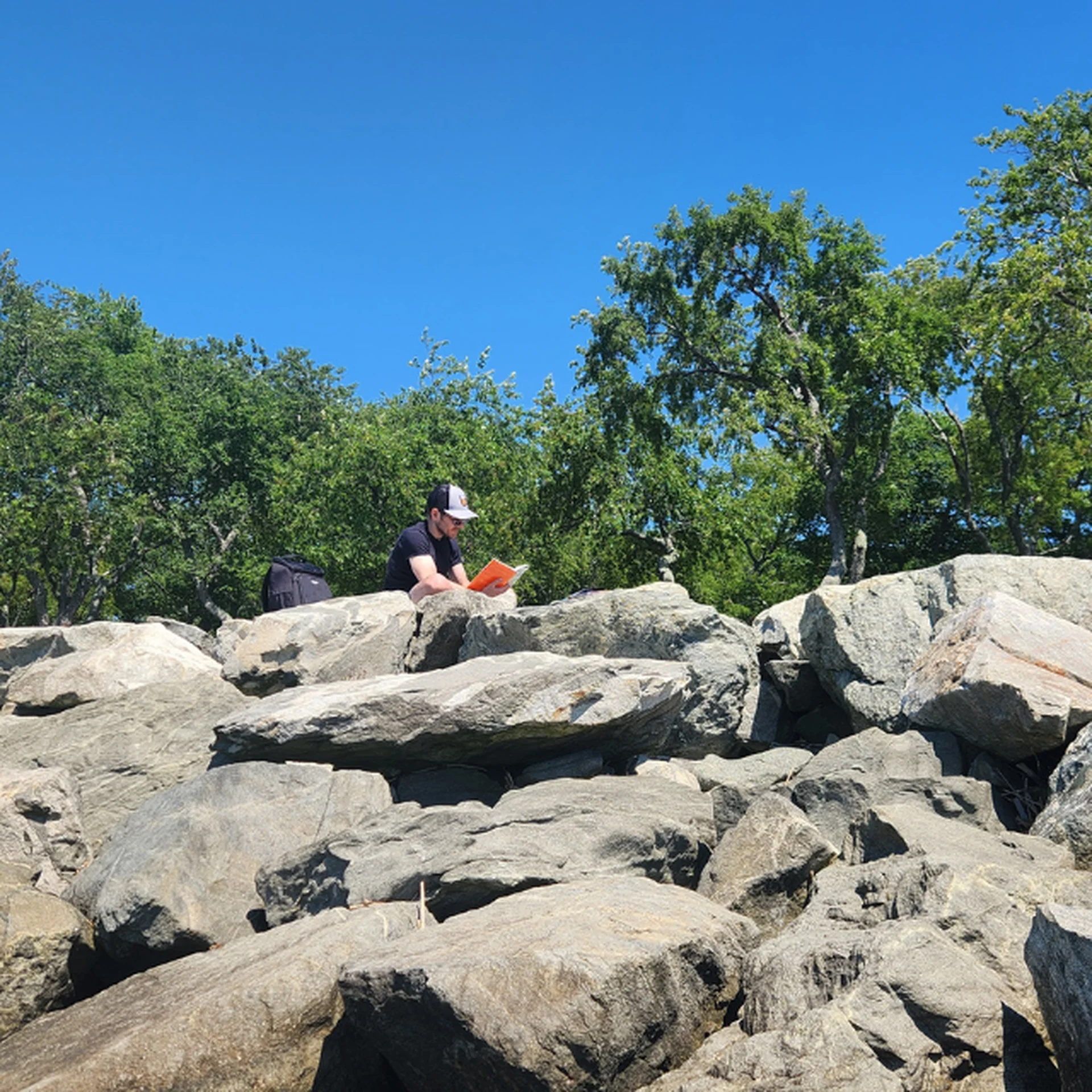 Alex sits atop a rocky beach, reading a book