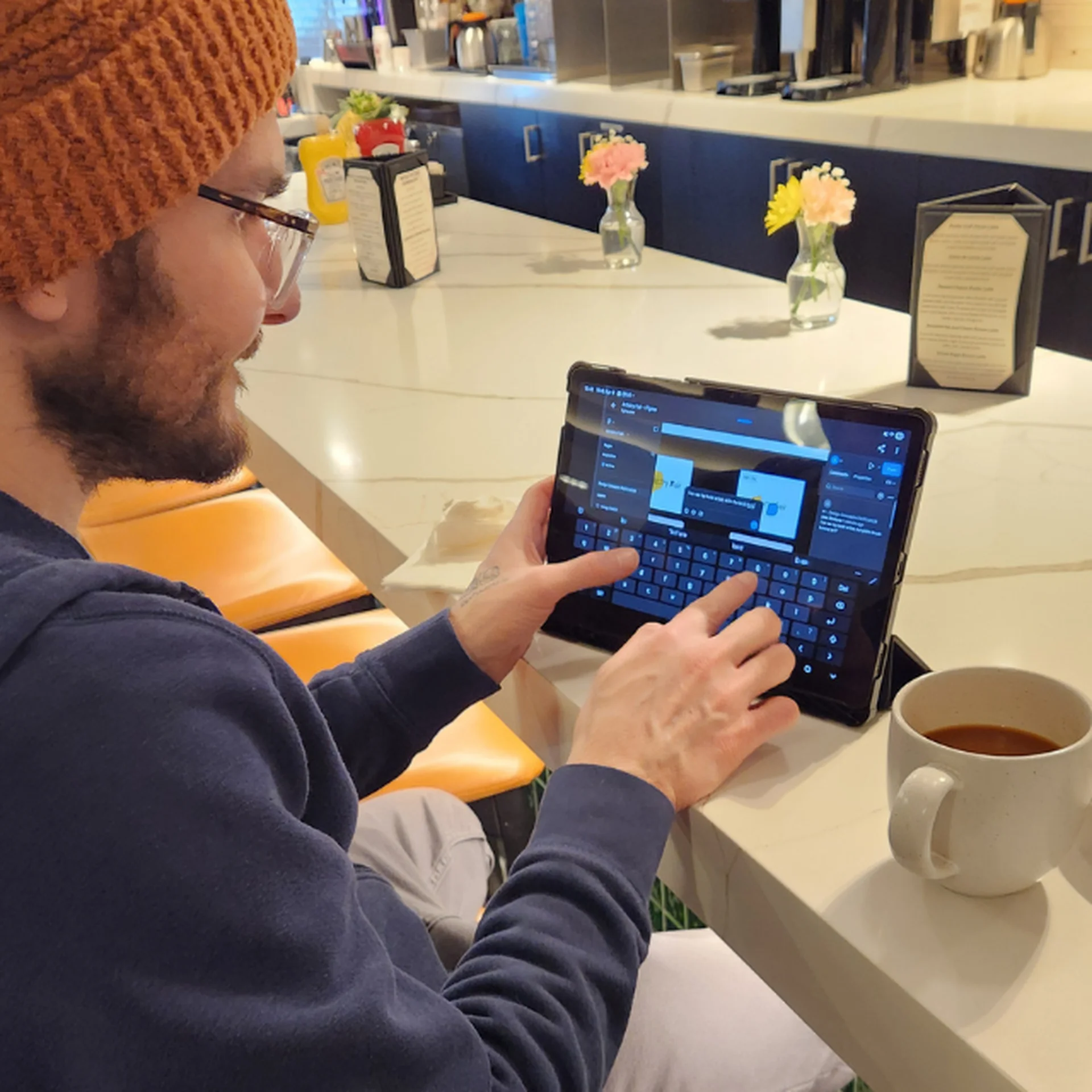 Alex sits in a cafe drinking coffee and working on Artistry Fair