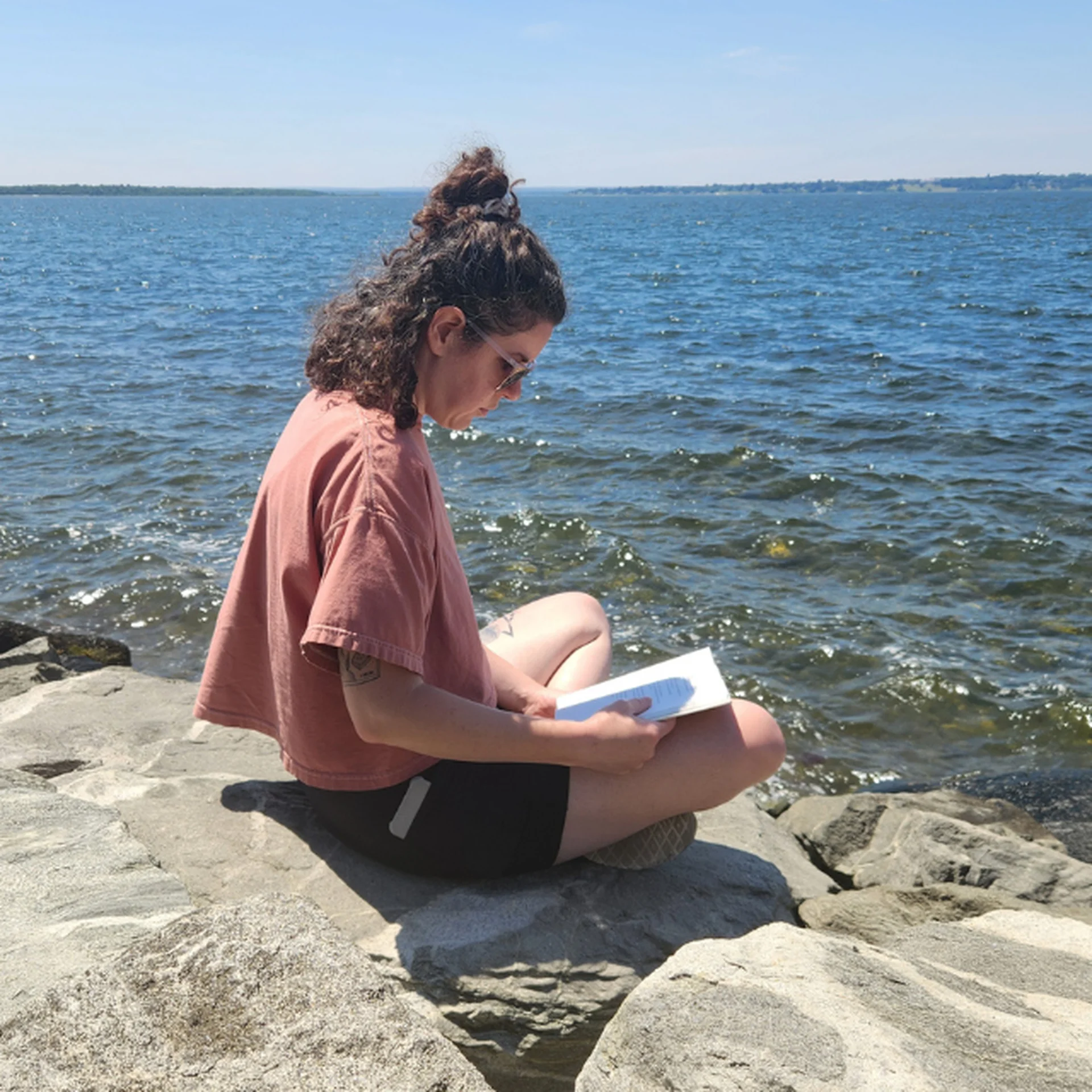 Person sits on a rock wall by the peaceful seaside and reads poetry